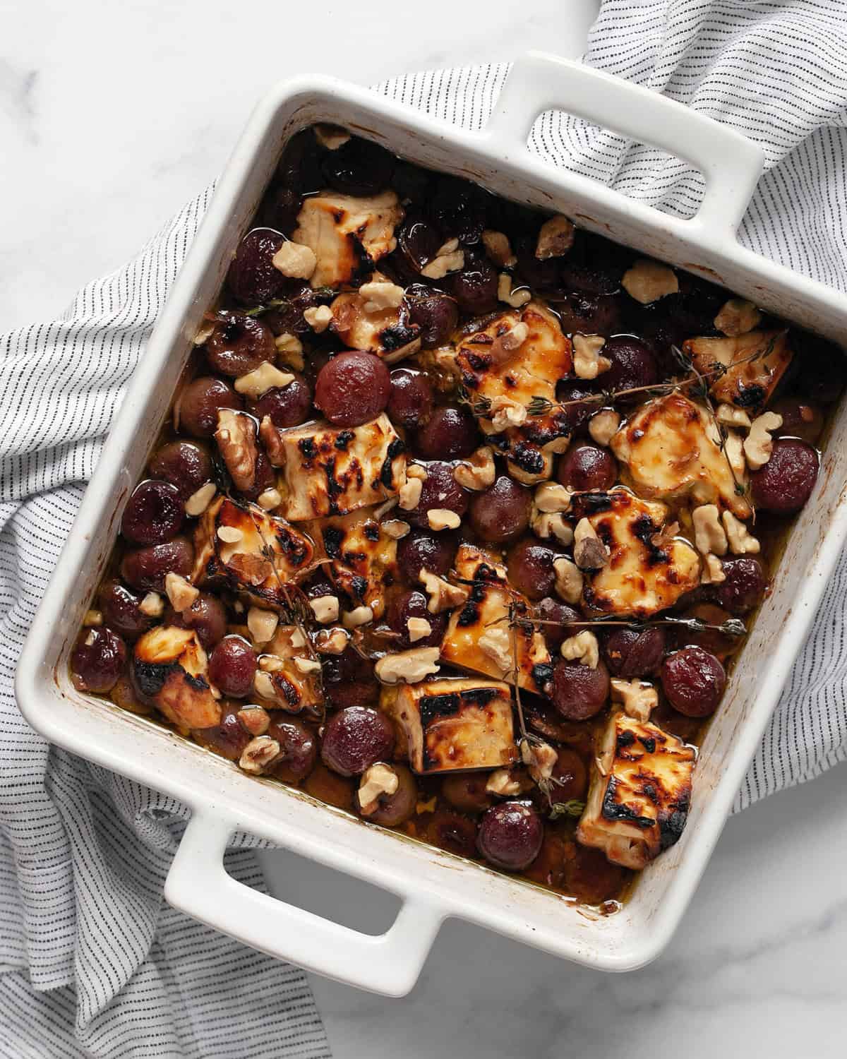 Baked feta and grapes in a dish with a serving spoon. 