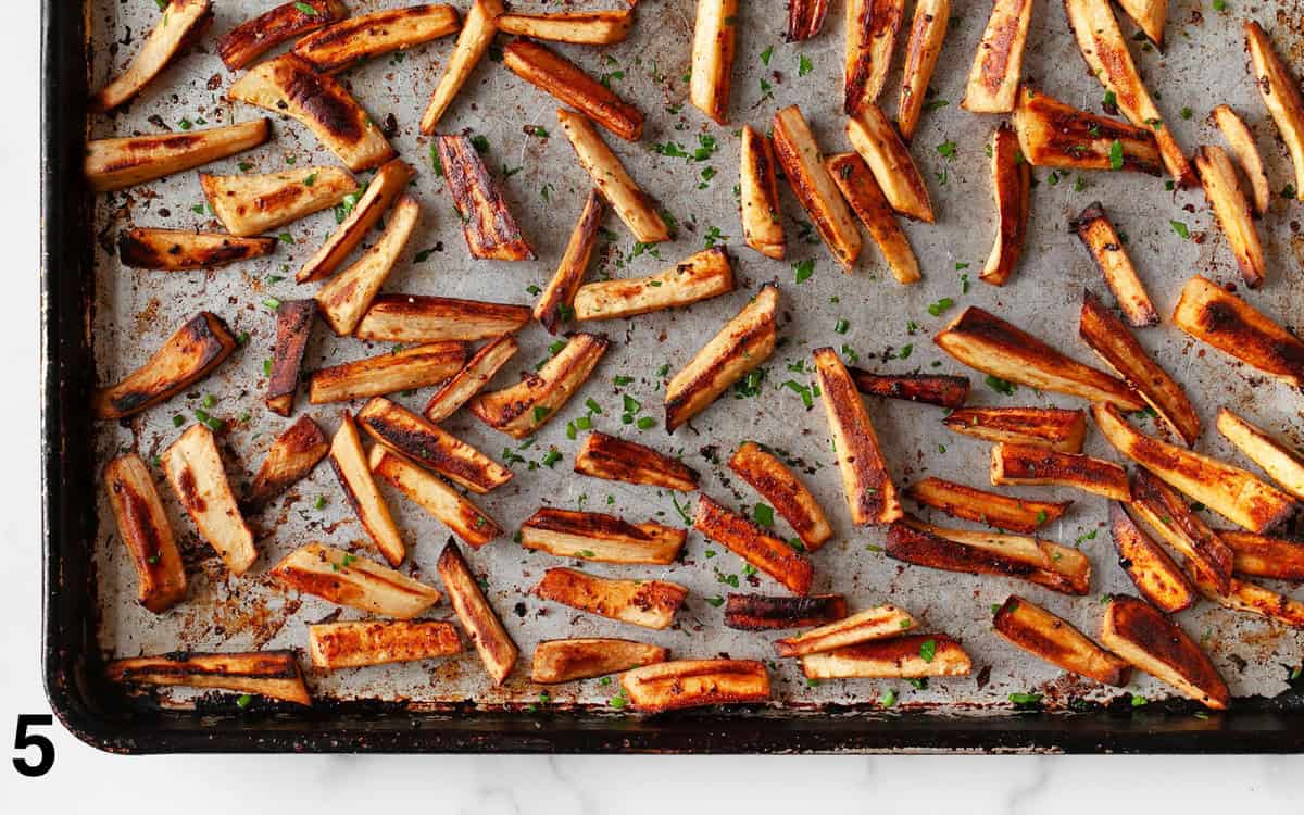 Roasted parsnips on a sheet on tossed with herbs.