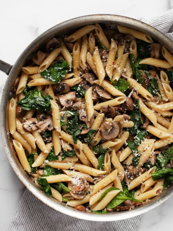 Penne pasta with mushrooms and spinach in a sauté pan.