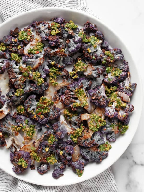 Roasted purple cauliflower on a plate drizzled with cilantro pesto.