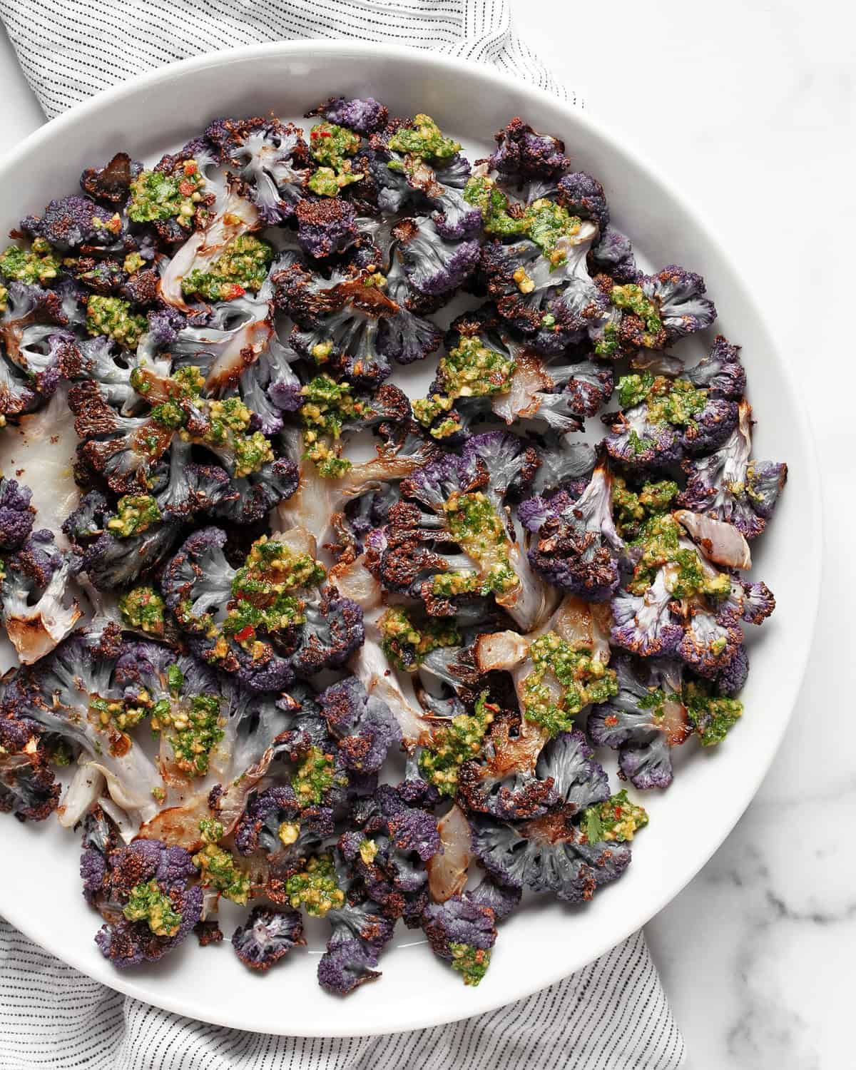 Roasted purple cauliflower on a plate drizzled with cilantro pesto.