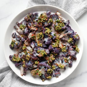 Roasted purple cauliflower on a plate drizzled with cilantro pesto.