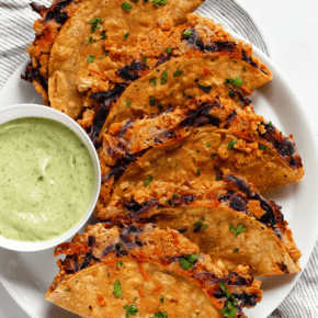 Baked crispy smashed chickpea tacos on a plate with avocado tahini sauce.