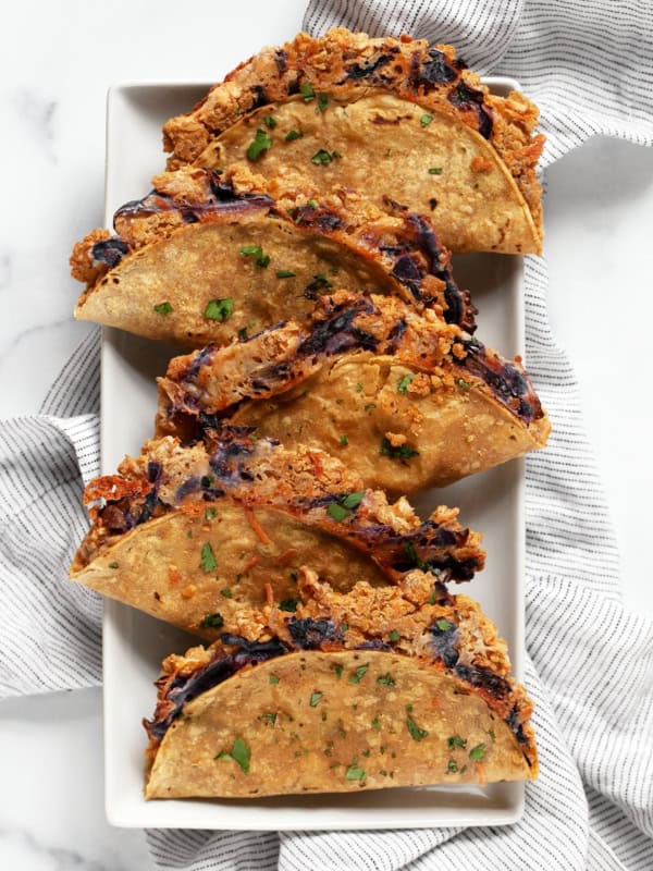 Baked crispy smashed chickpea tacos on a plate with avocado tahini sauce.