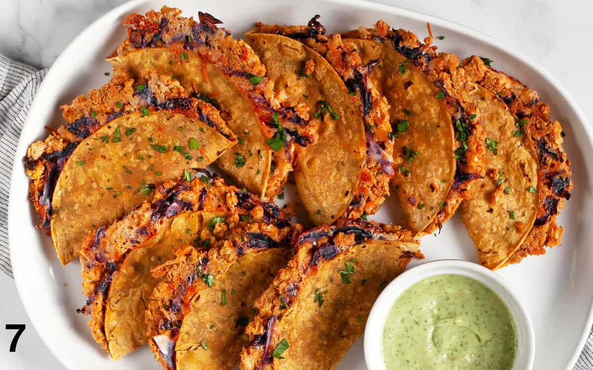 Crispy baked chickpea tacos on a plate with avocado tahini sauce in a small bowl.