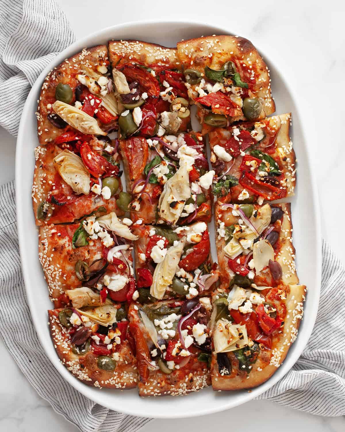 Mediterranean pizza cut into squares on a serving plate.