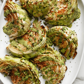 Roasted cabbage drizzled with tahini sauce on a serving platter.