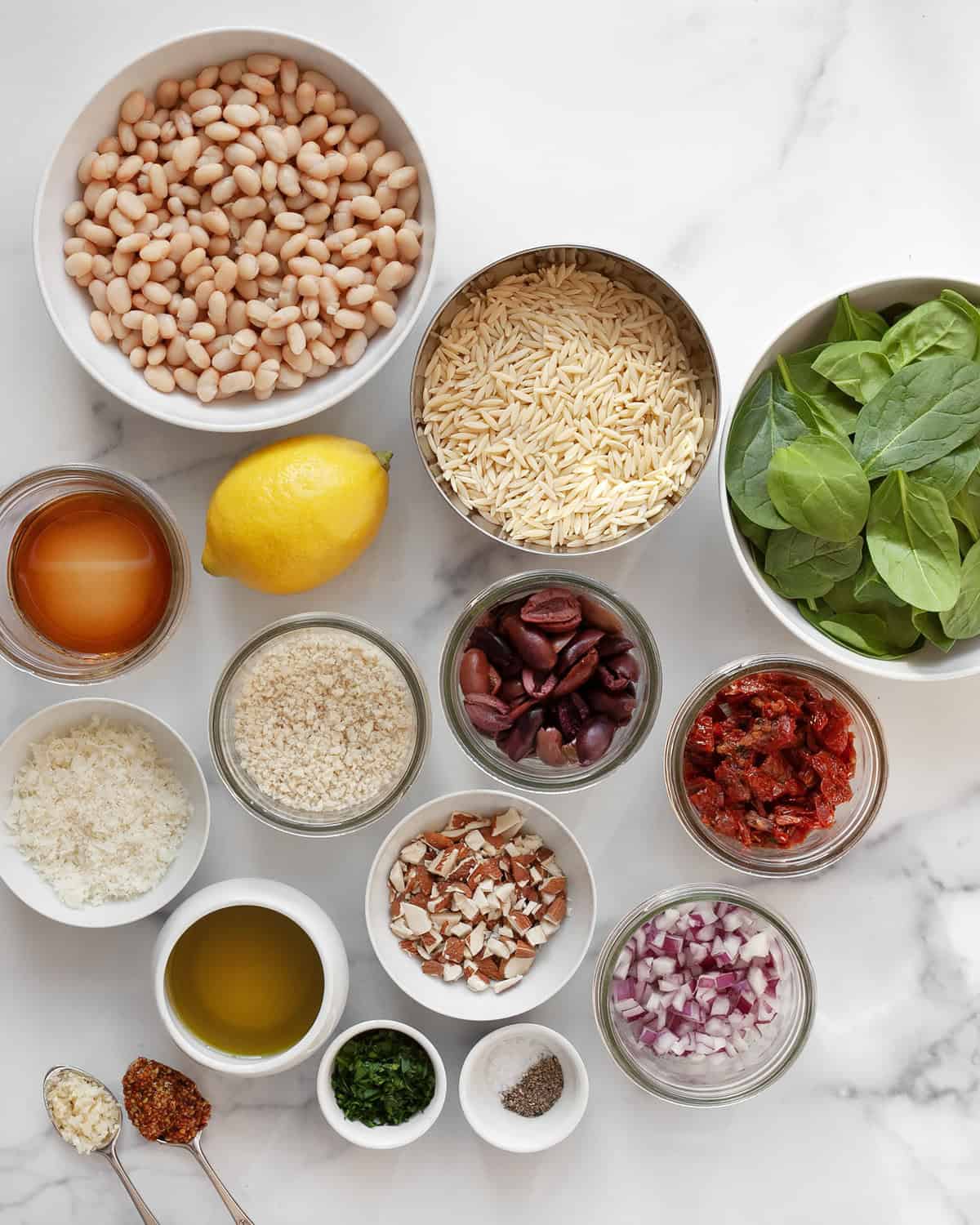 Ingredients including lemon, orzo, spinach, sun-dried tomatoes, olives, white beans, olive oil and garlic.