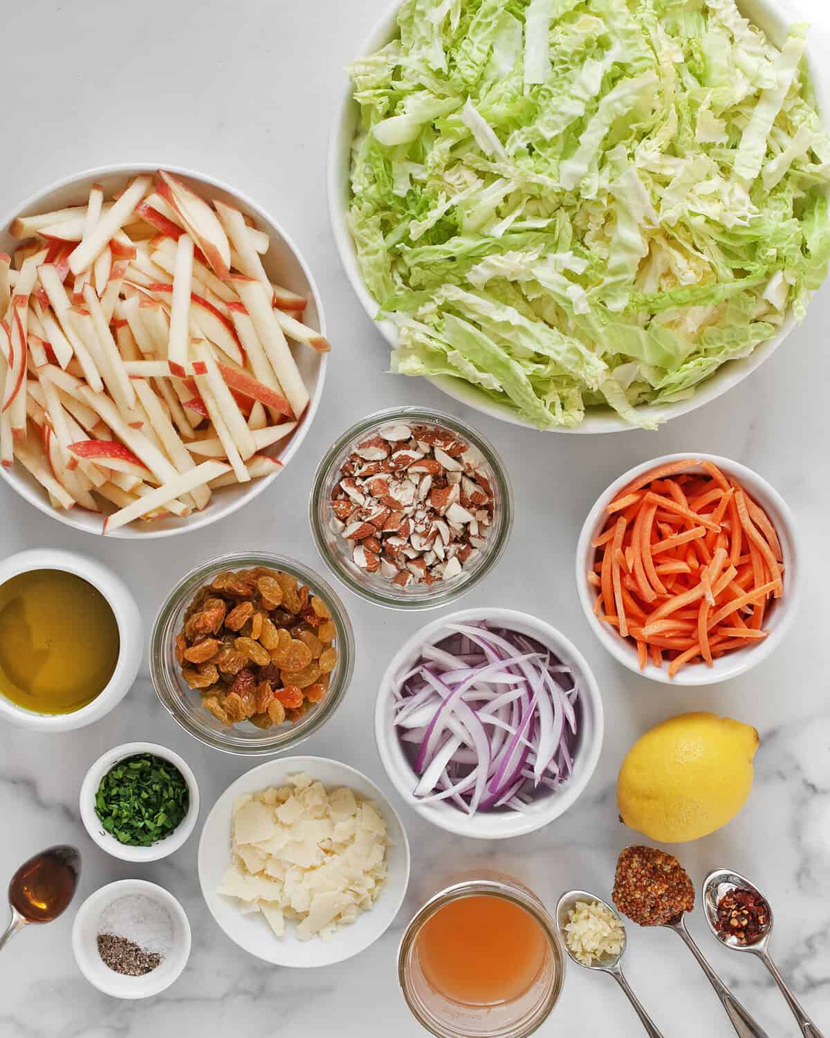 Ingredients including savoy cabbage, carrots, apples, almonds, red onions, raisins, apple cider vinegar, olive oil, mustard, garlic, salt, pepper, lemon and parsley.