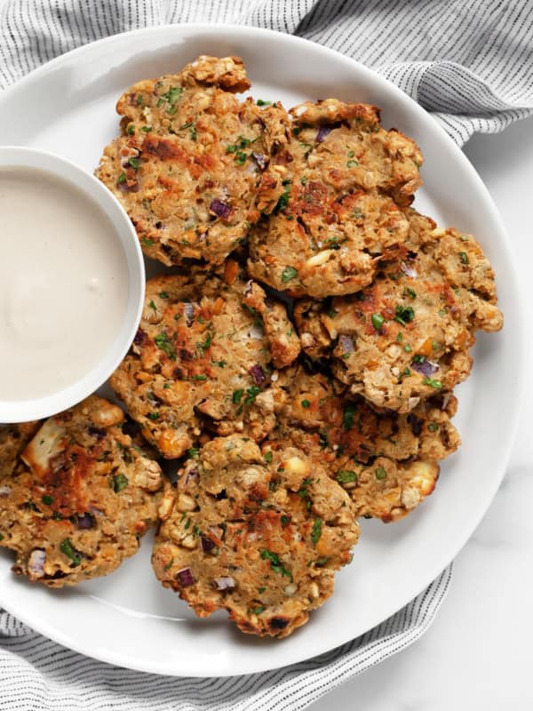 Baked chickpea fritters on a plate with a bowl of lemon tahini sauce.