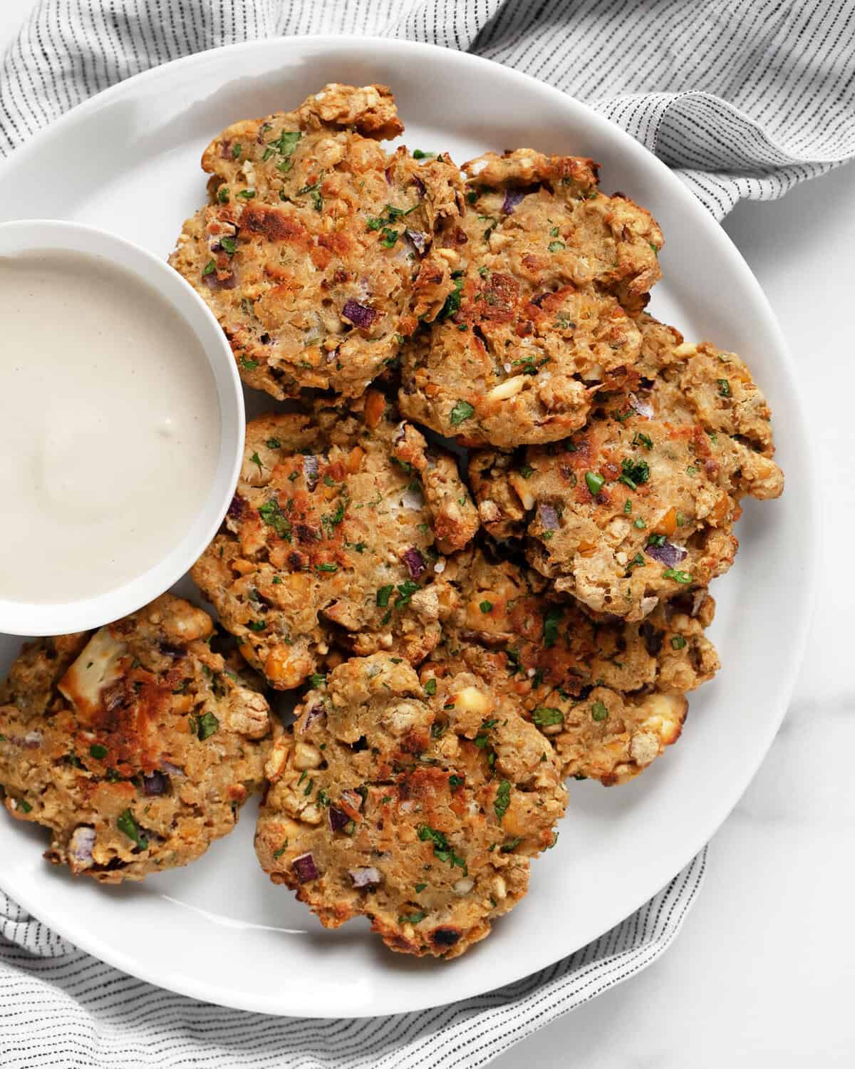 Baked chickpea fritters on a plate with a bowl of lemon tahini sauce. 