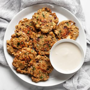 Baked chickpea fritters on a plate with a bowl of lemon tahini sauce.