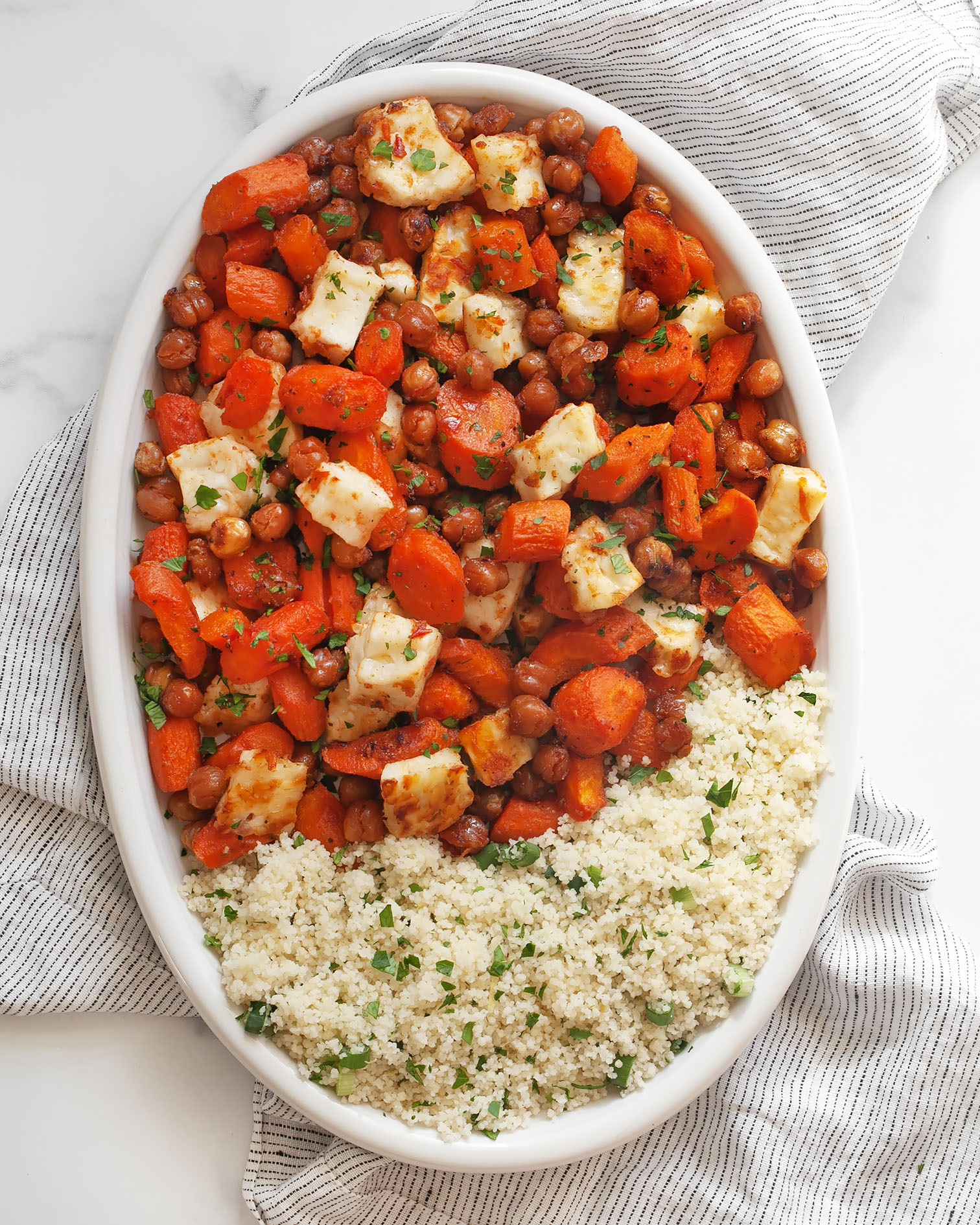 Harissa honey roasted carrots with chickpeas and halloumi with couscous on an oval serving platter.