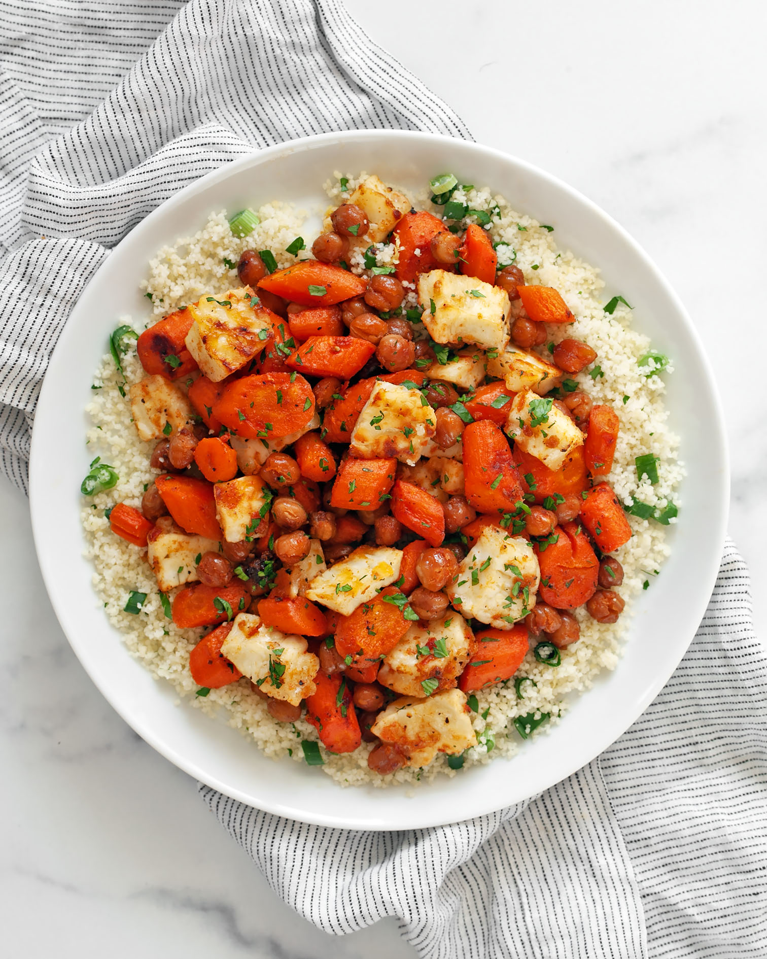 Harissa honey roasted carrots with chickpeas and halloumi on top of couscous on a plate.