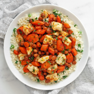 Harissa honey roasted carrots with chickpeas and halloumi on top of couscous on a plate.